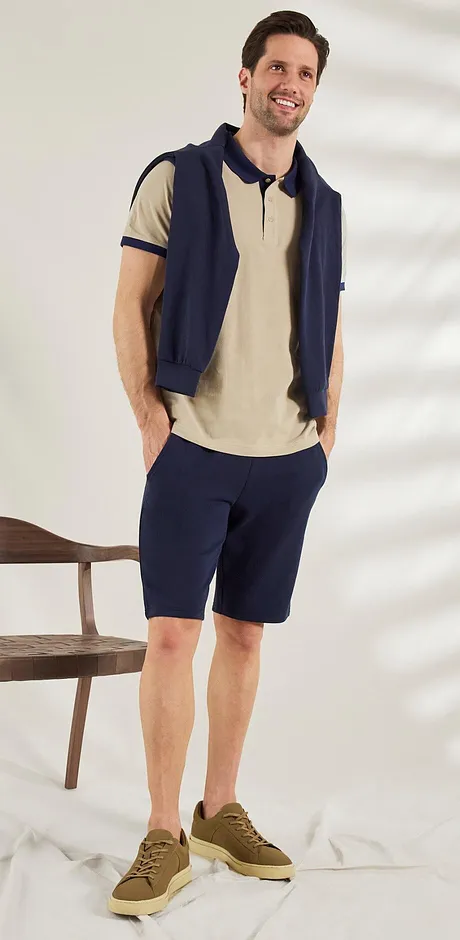Look estival décontracté : polo beige, gilet sans manches bleu foncé, sneakers marron. Tenue détente.