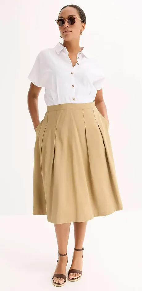 Look estival élégant : chemisier blanc à manches courtes associé à une jupe midi beige et des sandales noires.