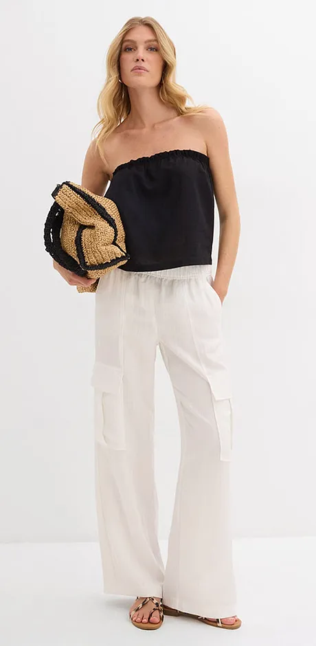 Tenue estivale avec top noir à épaules dénudées, pantalon en lin blanc et sac en paille. 