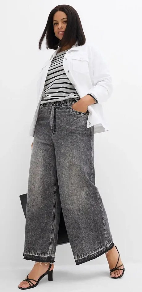 Jean large, top rayé et veste blanche pour un look moderne et décontracté.
