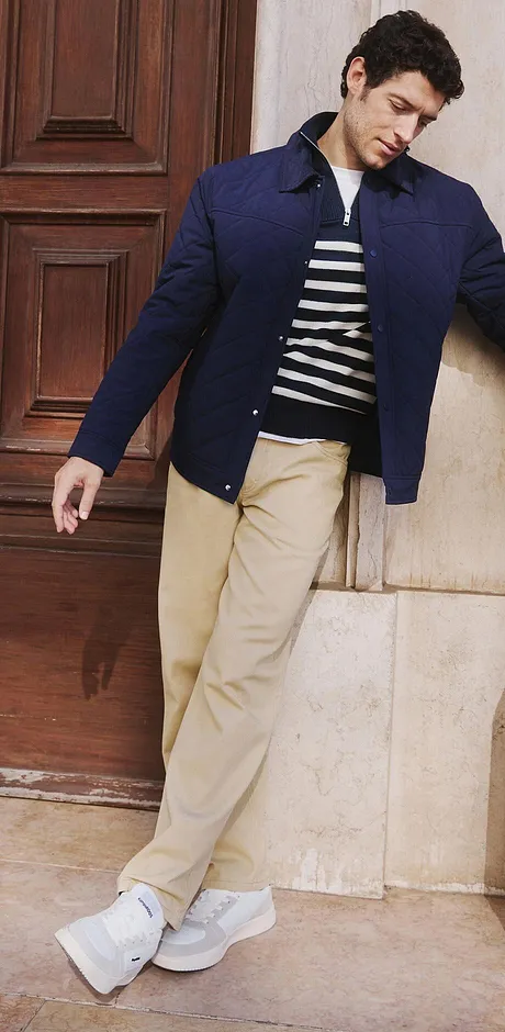 Une veste bleu foncé par dessus un haut rayé, pantalon beige et baskets blanches.