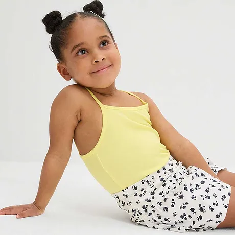 Top à bretelles jaune et jupe blanche à motif floral et pois noirs pour une tenue estivale.