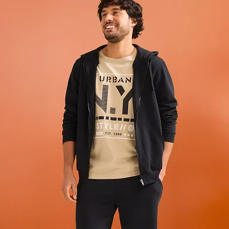 Look décontracté avec T-shirt beige, gilet noir à capuche & short en sweat foncé.