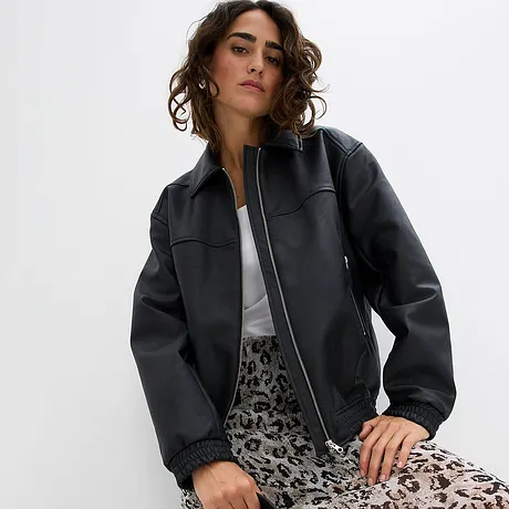 Veste noire enduite avec fermeture zippée, associée à un T-shirt blanc et une jupe à motifs.