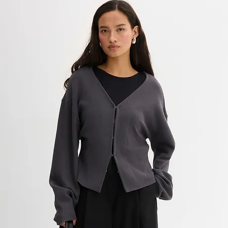 Gilet en maille gris élégant porté sur un top noir. Un look décontracté avec une encolure en V et une patte de boutonnage.