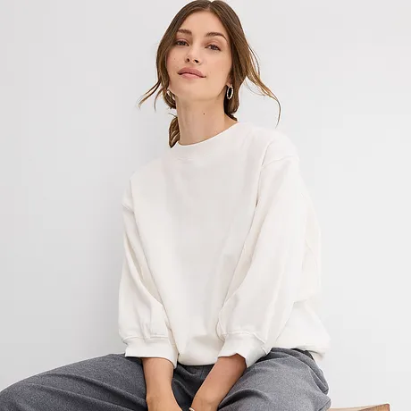 Sweat blanc oversize à manches amples, associé à un pantalon gris.