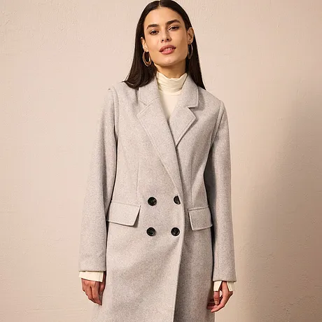 Manteau gris avec double rang de boutons, associé à un pull à col roulé de couleur crème.