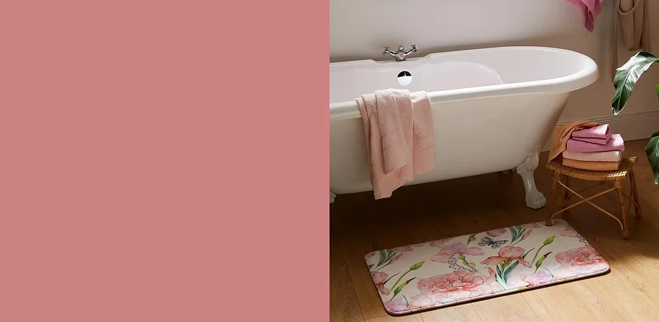 Des serviettes fraîches et un tapis de bain floral dans une salle de bain avec une baignoire vintage blanche.