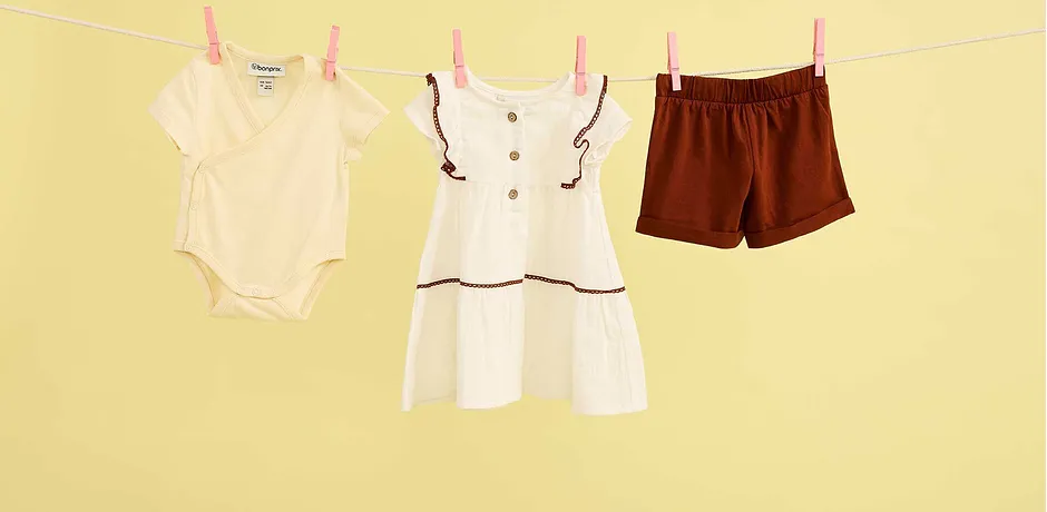 Vêtements d’été de bébé sur une corde à linge : body, robe blanche et short marron contre la chaleur.
