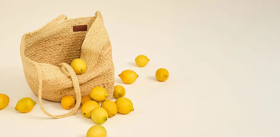Sac en paille tressée à anses, avec des citrons frais.