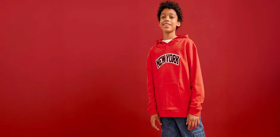Pull rouge à capuche avec inscription, jean bleu. Un look streetwear cool sur un fond rouge.