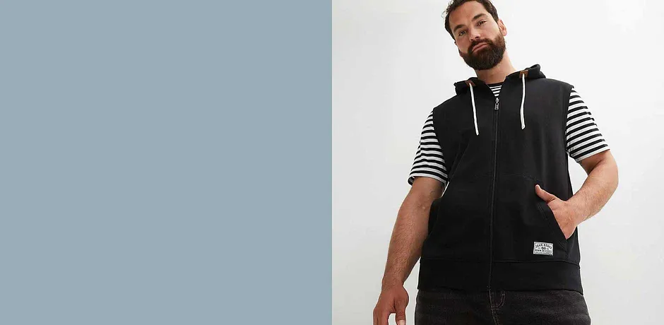 Gilet noir en sweat sans manches par dessus un T-shirt rayé.