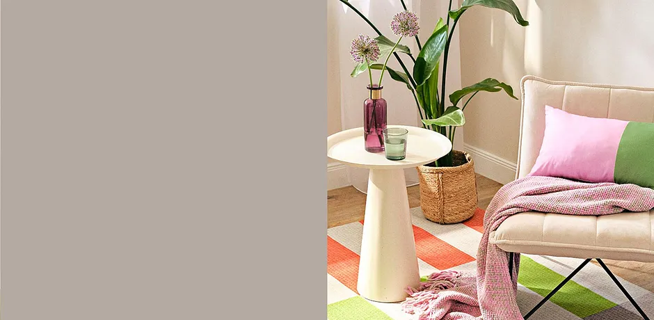 Des textiles en rose et vert pastel décorent un coin détente avec un plaid et un coussin sur un fauteuil.