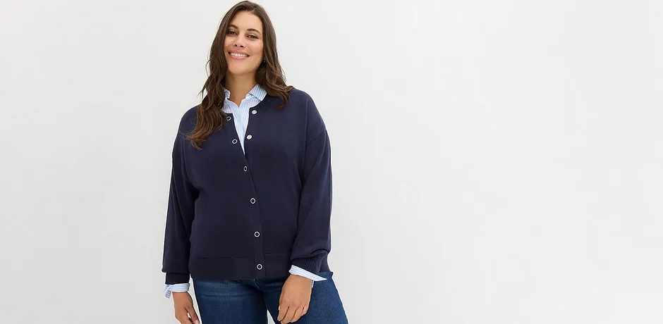 Gilet en maille bleu foncé par dessus un chemisier blanc, complété d'un jean classique.