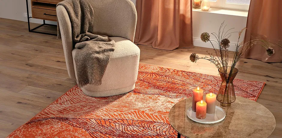 Fauteuil avec couverture douillette sur un tapis lumineux. Des teintes chaudes et automnales créent une ambiance cocooning. 