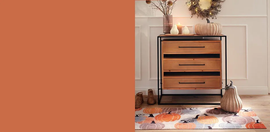 Commode en bois avec poignées noires, entourée d'objets de décoration d'automne dans des tons chauds et terreux.