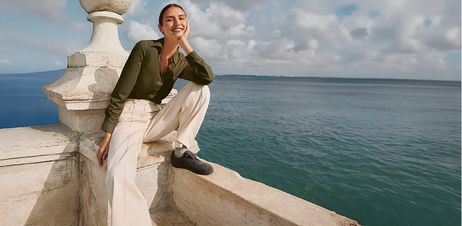 Chemisier vert olive, pantalon blanc ample et chaussures foncées.