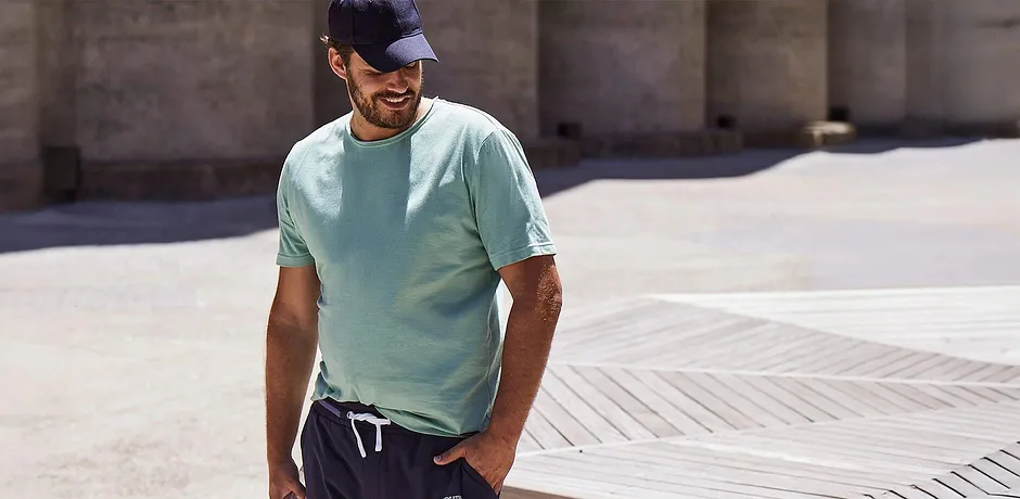 T-shirt couleur turquoise, pantalon foncé et casquette.